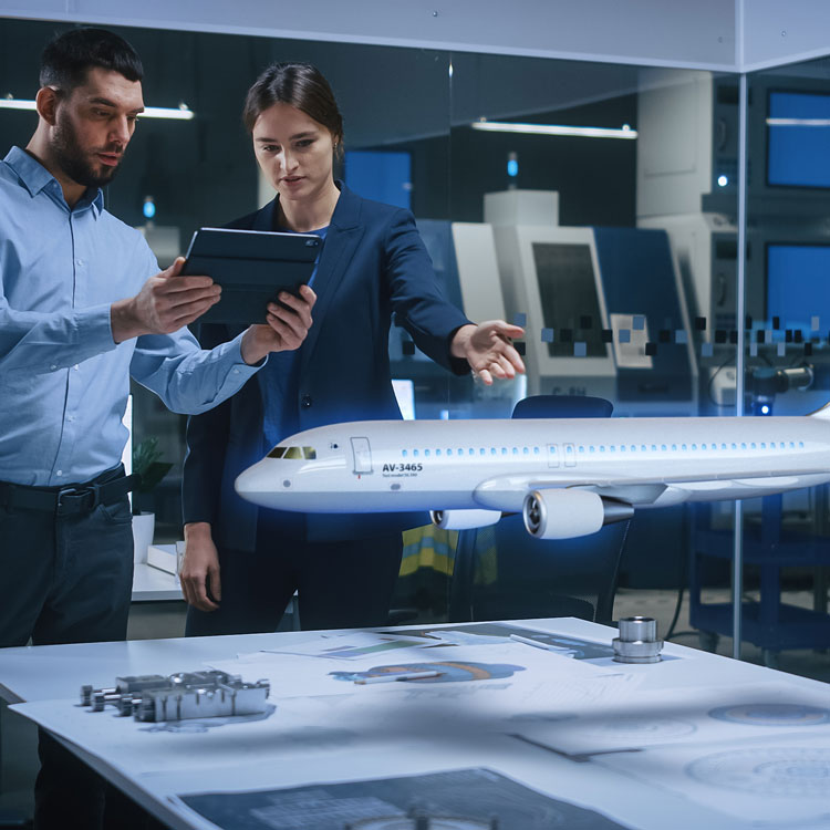 Aerospace engineers reviewing a tablet beside an aircraft model