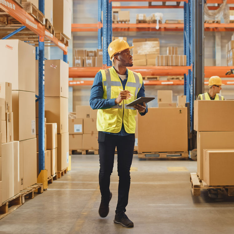 Warehouse worker with a tablet walking between stocked shelves